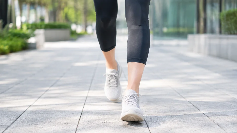 屋外の舗装路をスニーカーで歩く日本人女性の膝から下の足元(顔は写っていません)