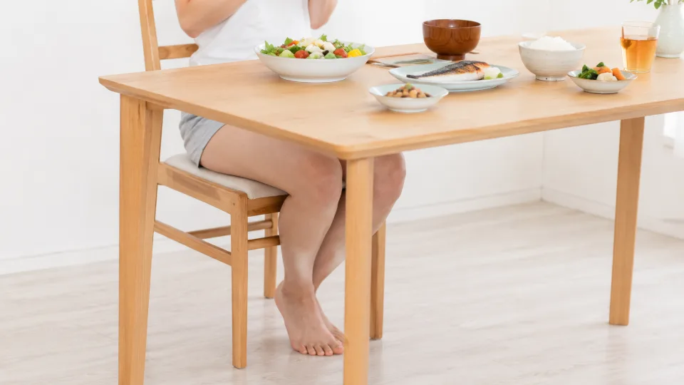健康的な和食が並ぶテーブルと、椅子に座る日本人女性の脚(顔は写していない)