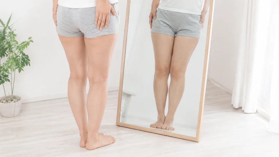 姿見(全身鏡)の前に立ち、自分の下半身のラインを確かめる日本人女性の脚(顔は写していない)